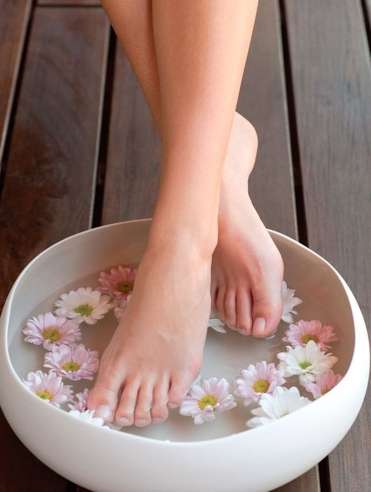 Relaxing herbal foot soak in white bowl with fresh daisy flowers
