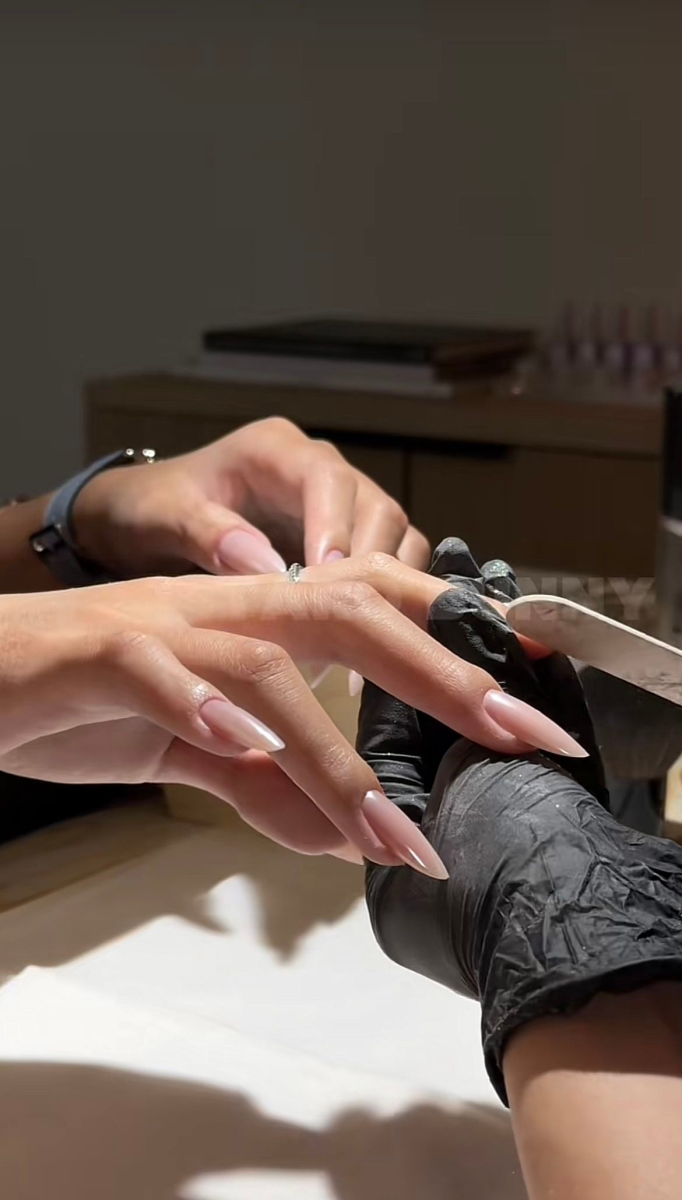 Nail technician shaping long nude stiletto nails with nail file